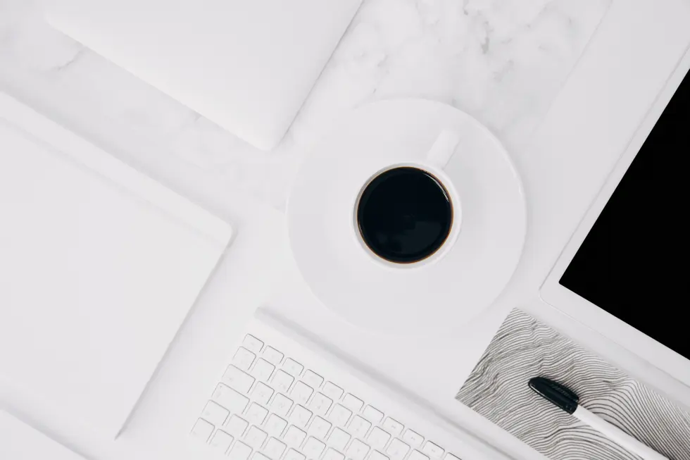 Arbeitsumgebung mit einer Tasse schwarzem Kaffee auf einem weißen Teller, umgeben von einem weißen Laptop, einem Notizbuch, einer Tastatur und einem Tablet. Die gesamte Szene auf einem marmorierten Tisch vermittelt einen minimalistischen und modernen Eindruck, ideal für kreatives Arbeiten oder eine produktive Schreibsession.
