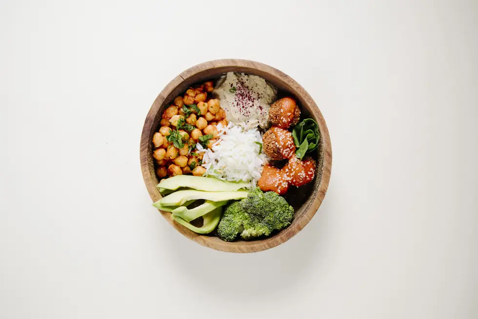 Schüssel mit Hirse-Bowl, gedünstetem Gemüse, Kichererbsen, Avocado, Reis, frischen Kräutern und Hummus, serviert in einer Holzschüssel, die eine gesunde, FODMAP-arme und glutenfreie Mahlzeit darstellen.