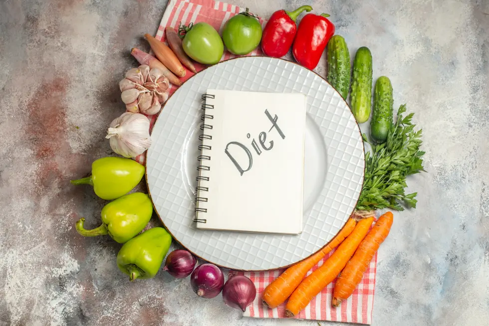 Mediterrane Bowl mit frischem Gemüse, Hülsenfrüchten und Lachs, umgeben von einem Notizbuch mit der Aufschrift "Diet". Die Komposition zeigt eine Vielzahl von Zutaten, darunter grüne und rote Paprika, Gurken, frische Kräuter, Karotten, Zwiebeln und Knoblauch, auf einem eleganten Teller. Ideal zur Visualisierung gesunder Ernährung undMeal Prepping.