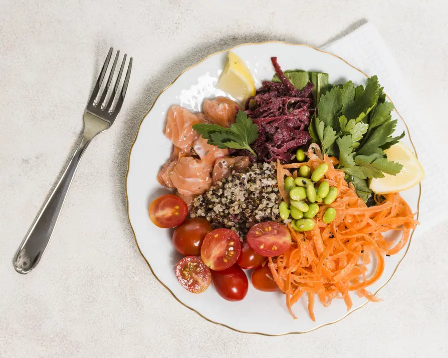 Ausgewogener Teller mit Lachs, Quinoa, Karottenraspeln, Edamame, Cherrytomaten und frischen Kräutern, garniert mit Zitrone, auf hellen Untergrund. Ideal für gesunde Ernährung und Stoffwechselstabilisierung gemäß InYologie-Prinzipien.