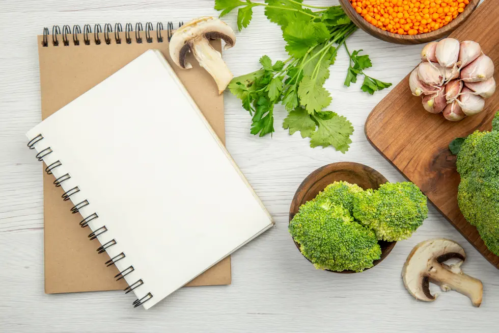 Gesundes Rezeptset-Up mit einem leeren Notizbuch auf einem rustikalen Holzuntergrund, umgeben von frischem Gemüse wie Brokkoli, Koriander, Knoblauch und Pilzen sowie einer Schale mit roten Linsen. Ideal für die Planung nährstoffreicher Mahlzeiten und kreative Rezeptideen.