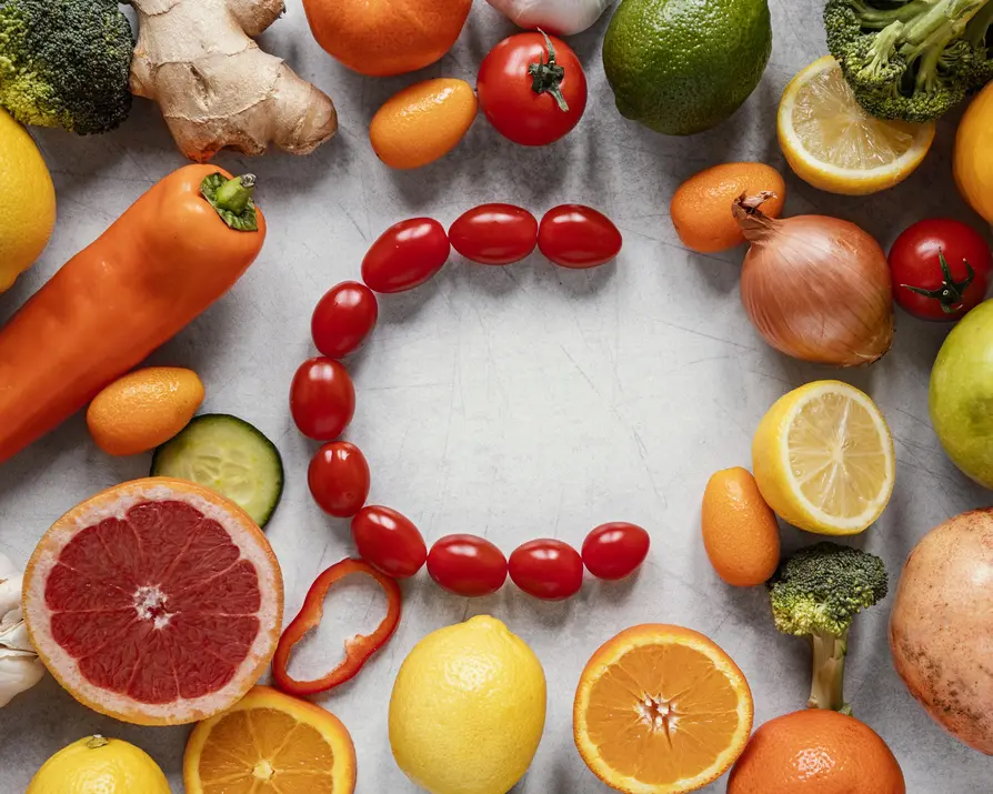Bunte Auswahl an frischem Obst und Gemüse, darunter Paprika, Kirschtomaten, Zitrusfrüchte und Brokkoli, präsentiert auf einer grauen Arbeitsfläche. Die lebendigen Farben und Formen wecken Interesse und vermitteln eine gesunde Ernährung. Die Anordnung der Lebensmittel in der Form eines "C" symbolisiert eine bewusste Wahl für eine nährstoffreiche, low-FODMAP Ernährung zur Unterstützung der Darmgesundheit und Bekämpfung von Stoffwechselblähungen.